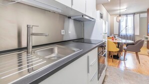 Een moderne keuken met een roestvrijstalen spoelbak, een inbouwoven en een eethoek met een tafel en stoelen.