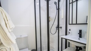 A modern bathroom with a glass-enclosed shower, a white toilet, a sink with a mirror, and a towel rack.
