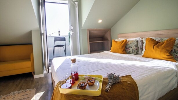 A hotel room with a bed, a yellow sofa, a tray with food and drinks, and a view of the outside.