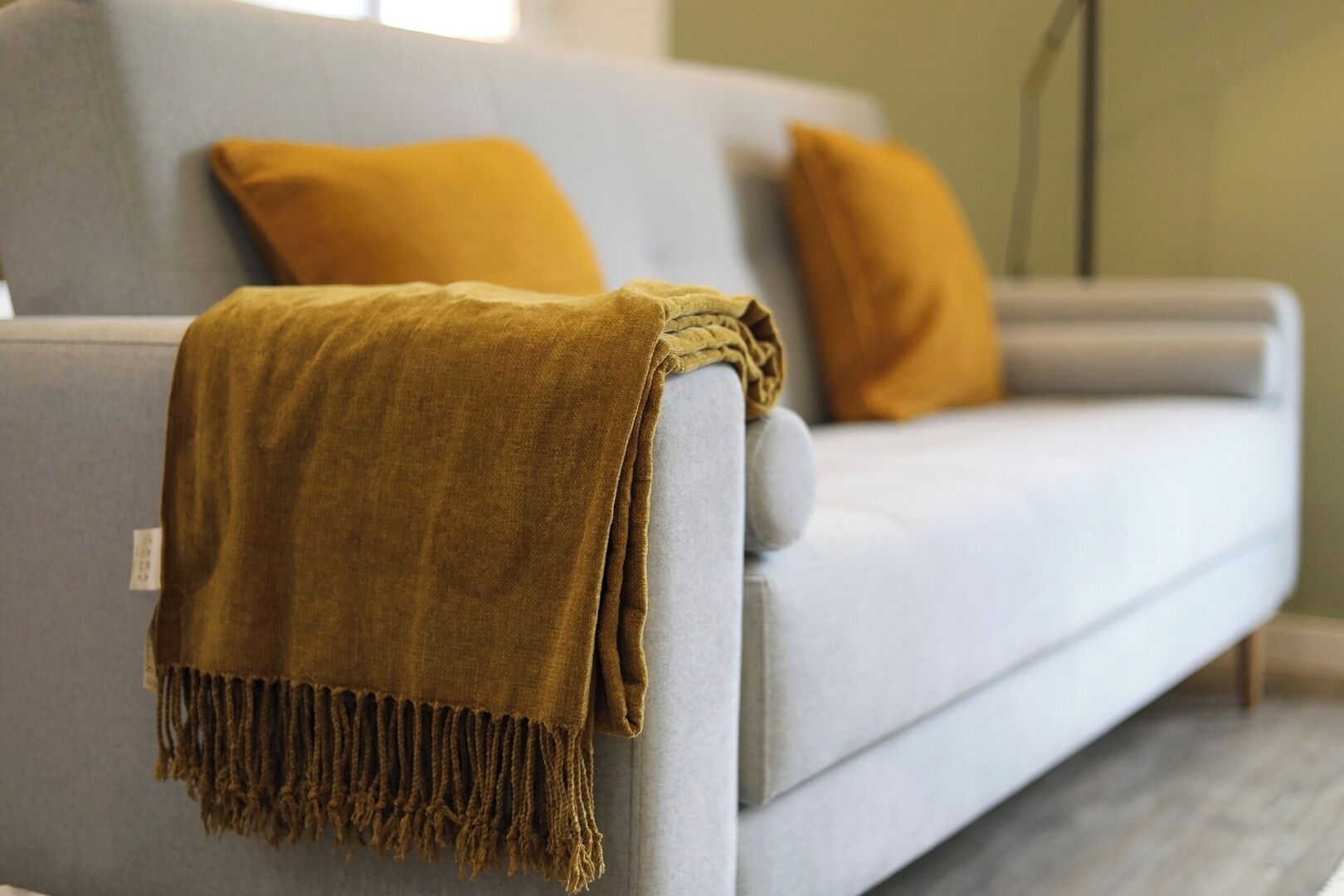 A modern sofa with a mustard-colored throw blanket and matching cushions.