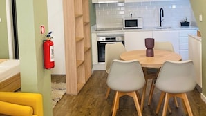A compact kitchen with white cabinets, a microwave, and a sink. There is a dining table with four chairs and a fire extinguisher mounted on the wall. - Loios Suites and Apartments (Lisbon)