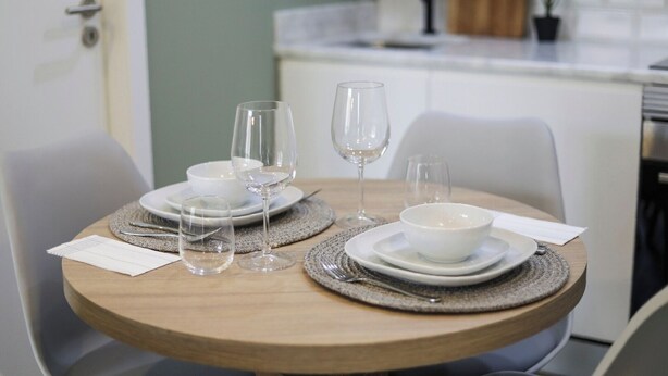 A dining table set with white plates, bowls, and wine glasses, surrounded by chairs. - Loios Suites and Apartments (Lisbon)