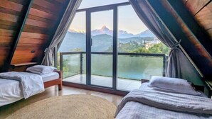 Una habitación con dos camas, un amplio ventanal que da a un balcón y vistas a las montañas.