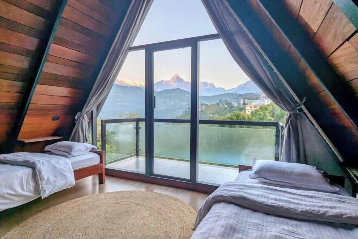 A room with two beds, a large glass door leading to a balcony, and a view of mountains.