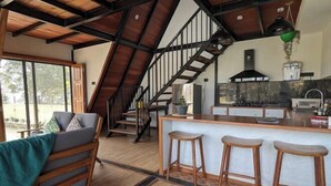 Una cocina moderna con una isla central, taburetes de bar y una escalera que sube a un nivel superior.