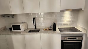 A modern kitchen with white cabinets, a stainless steel sink, a microwave, a coffee maker, and an oven.