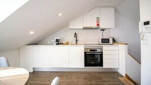 Une cuisine moderne avec des meubles blancs, un four à micro-ondes, un four traditionnel et une machine à café.