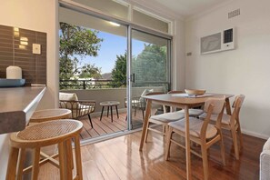 A dining area with a table and chairs, a sliding glass door to an outdoor deck, and a kitchen counter with a bowl and a vase. - Cosy and Quiet Walk to Beach and Harbor (Rose Bay)