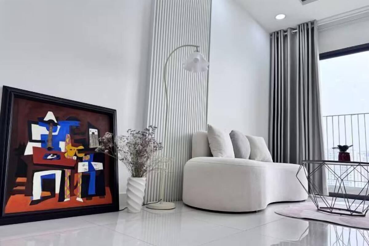 Un salon moderne avec un canapé blanc, un tableau abstrait encadré, un grand lampadaire et une vue sur la ville à travers de grandes fenêtres.