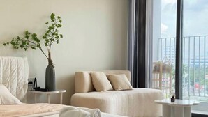 A hotel room with a bed, a sofa, a small table, a vase with a plant, and a balcony with a view.