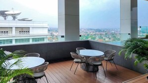 Une terrasse moderne sur le toit, offrant une vue panoramique sur la ville, avec une table ronde, des chaises en osier et de grandes fenêtres.