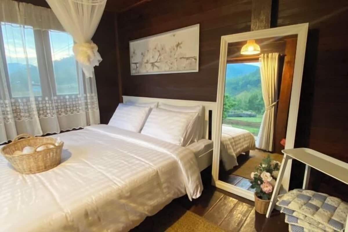 A bedroom with two beds, a wicker basket on the left bed, a painting on the wall, and a view through an open door.