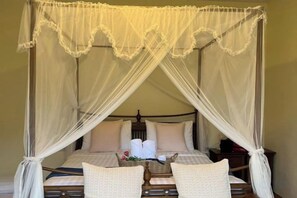 Una cama con dosel sobre cuatro columnas, con estructura de madera y ropa blanca.