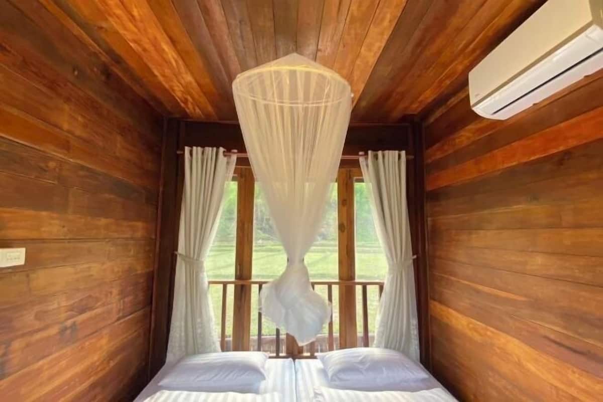 A wooden cabin room with a bed, a mosquito net, and an air conditioning unit.