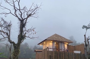 Una pequeña cabaña de madera con techo de paja, rodeada de árboles y una cerca de madera.
