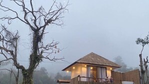 A wooden cabin with a thatched roof, a balcony with a white bathtub, and a view of the surrounding forest. - Chan Rak Khao Villa (Bo Kluea)