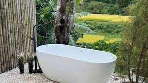 A white freestanding bathtub in a garden setting with a bamboo fence, potted plants, and a view of a rice field. - Chan Rak Khao Villa (Bo Kluea)