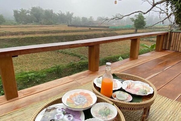 Una terraza de madera con una mesa dispuesta para una comida, con vista a un campo de arroz.