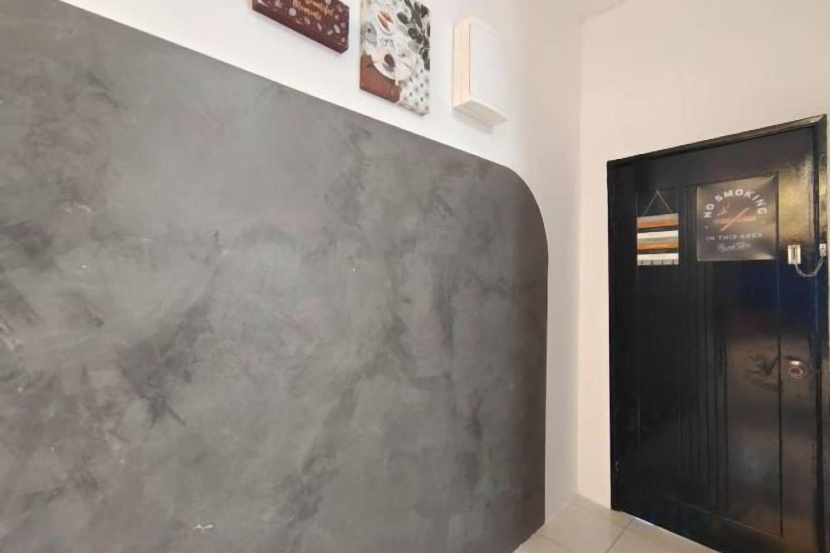 Un couloir avec un mur gris à texture et une porte noire portant une inscription.
