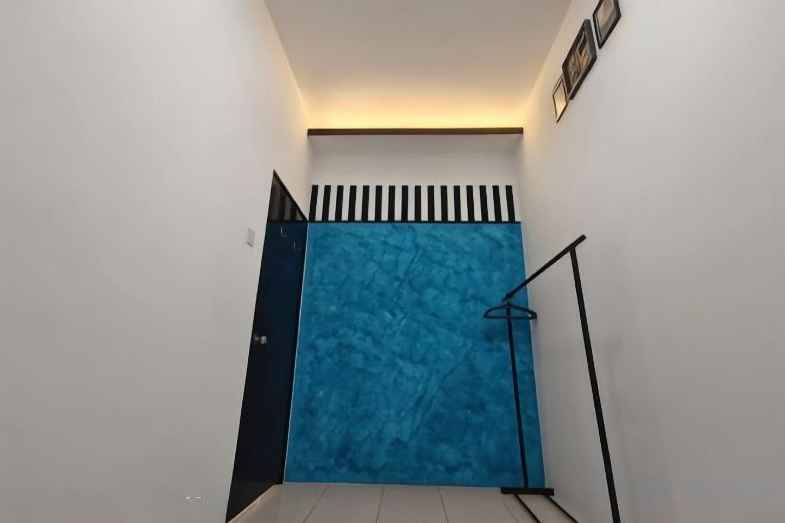 Un escalier étroit avec un mur bleu à texture, une main courante en métal noir et une porte noire en haut.