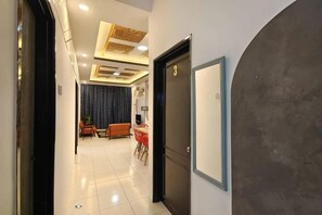 A hotel hallway with a door, a dining area with chairs and a table, and a large mirror on the wall. - Ifloral CH1 (Tanah Rata)