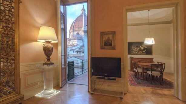 A room with a TV, a lamp, a dining area with chairs, a table, and a view of a dome building. - Yome - Your Home in Florence (Florence)