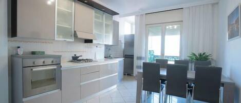 A modern kitchen with stainless steel appliances, a dining area with a table and chairs, and a large window providing natural light.