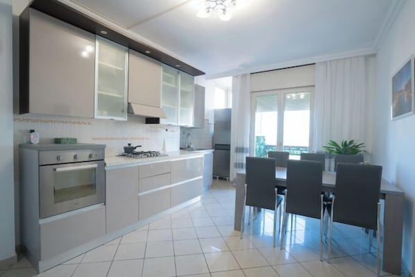 A modern kitchen with stainless steel appliances, a dining area with a table and chairs, and a large window providing natural light.