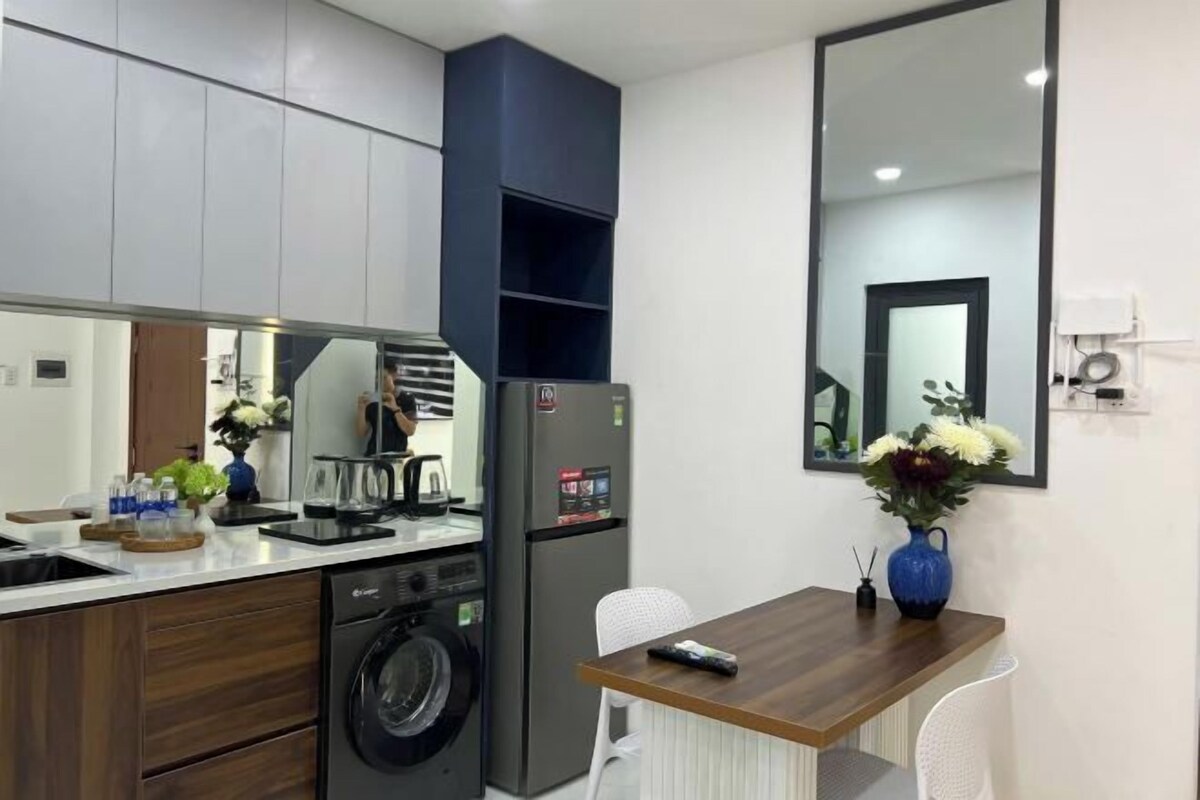 Een compacte keuken met een wasmachine, een koelkast, een eettafel met stoelen en een grote spiegel.