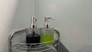 Ein Badezimmer im Eck mit einem Metallregal, auf dem zwei Glasbehälter stehen, einer mit dunkler Flüssigkeit und der andere mit grüner Flüssigkeit.