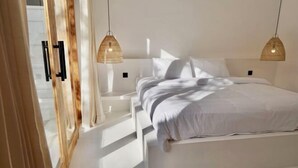 A modern bedroom with a large bed, two pendant lights, and a wooden door. - Villa Enda (Bali)