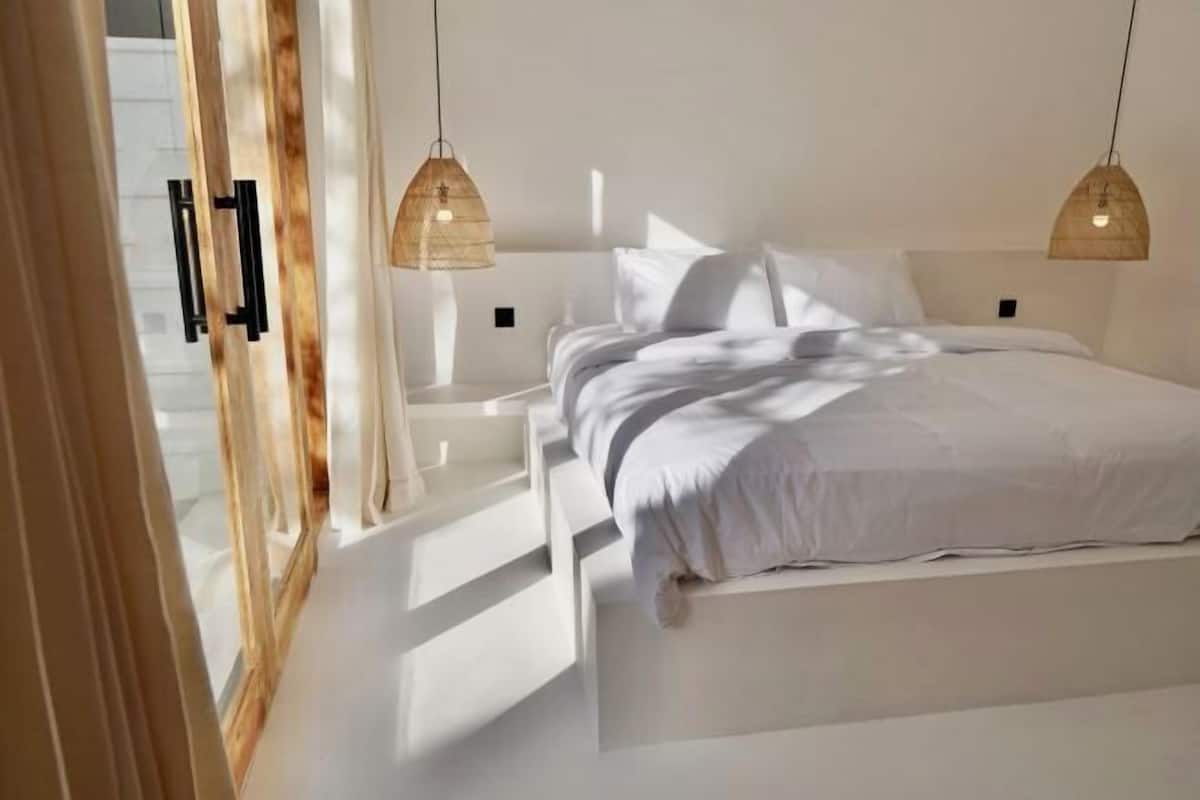 Une chambre moderne avec un grand lit, deux lampes suspendues et une porte en bois.