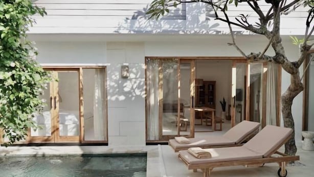 A modern outdoor pool area with two lounge chairs and a glass-enclosed dining area. - Villa Enda (Bali)