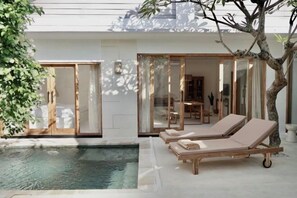 A modern outdoor pool area with two lounge chairs and a glass-enclosed dining area. - Villa Enda (Bali)