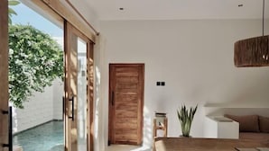 A modern interior with a wooden dining table, a white sofa, and a view of a swimming pool. - Villa Enda (Bali)