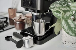 A coffee machine with a cup placed underneath, a measuring spoon, a small container, and a plant in the background. - Villa Enda (Bali)