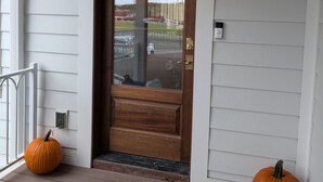 A wooden front door with a glass panel, a porch with wooden steps, and two pumpkins on the ground.