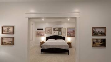 A bedroom with a bed centered in the room, flanked by framed pictures on the walls, and a carpeted floor.
