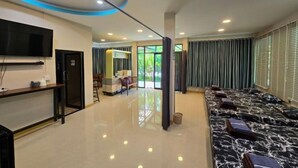 Um hall de hotel com balcão de recepção, uma TV, área de estar com sofá estampado e uma janela grande com cortinas.