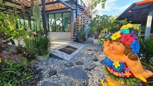 Uma casa moderna com fachada de vidro, pérgola de madeira e um jardim com estátuas decorativas.