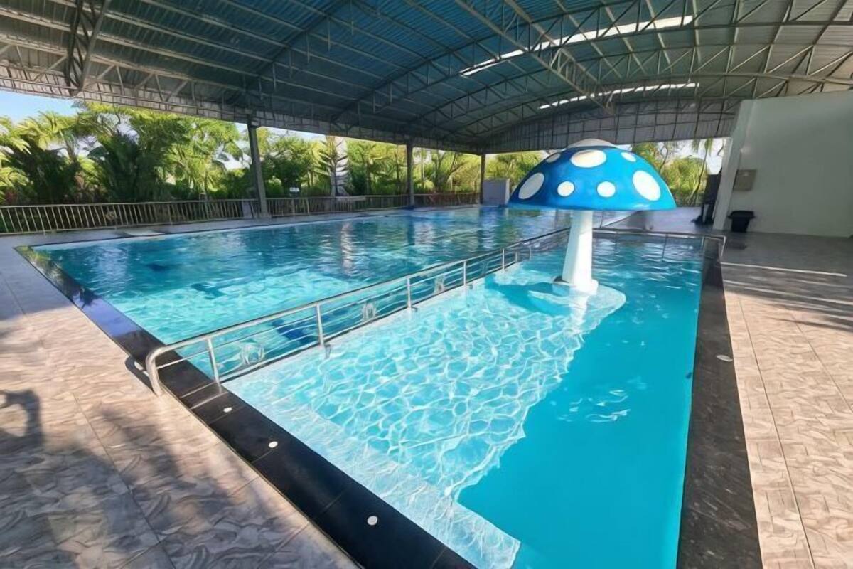 A swimming pool with a blue and white mushroom decoration, a covered roof, and a tiled floor.