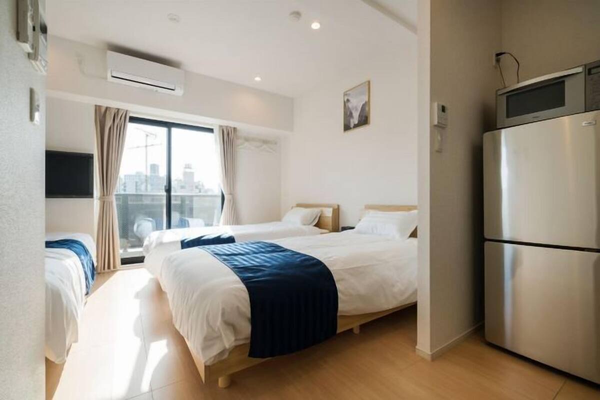 Une chambre d’hôtel avec deux lits, une grande fenêtre avec des rideaux, un réfrigérateur et un appareil de climatisation.