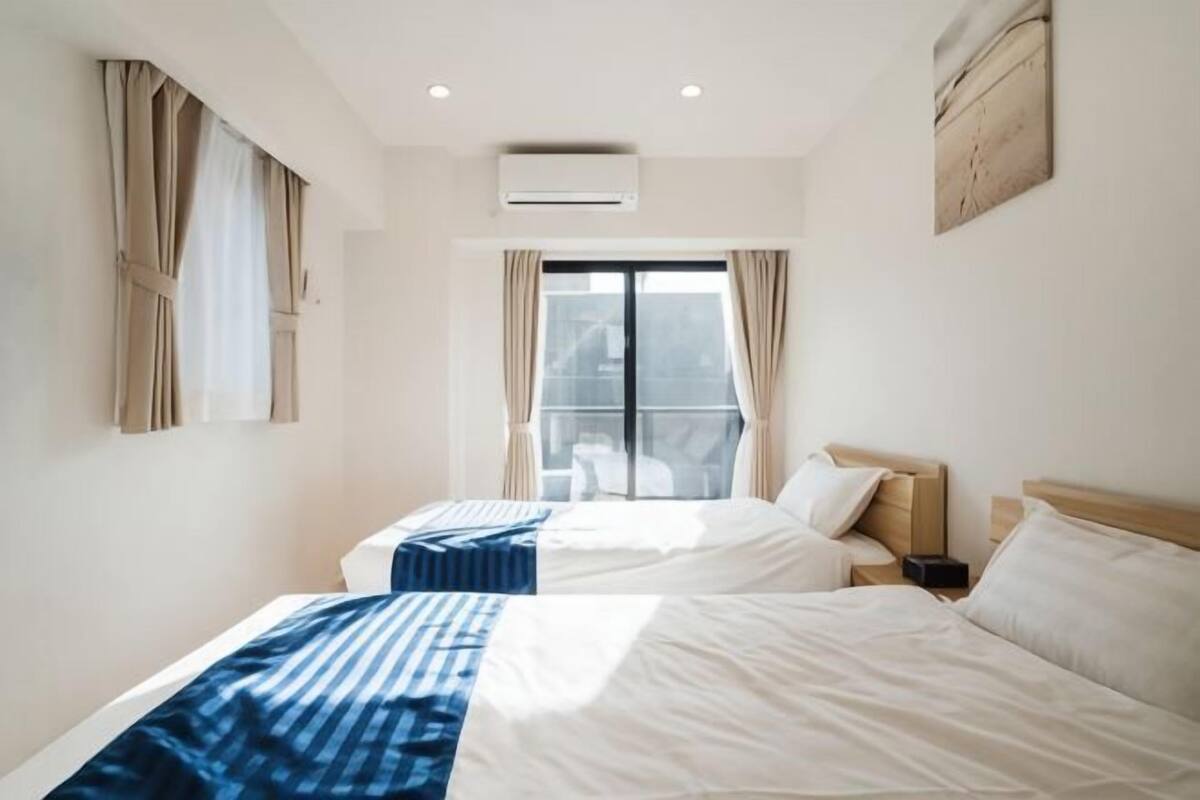 Une chambre d’hôtel avec deux lits, une fenêtre avec des rideaux, un appareil de climatisation et une œuvre d’art accrochée au mur.