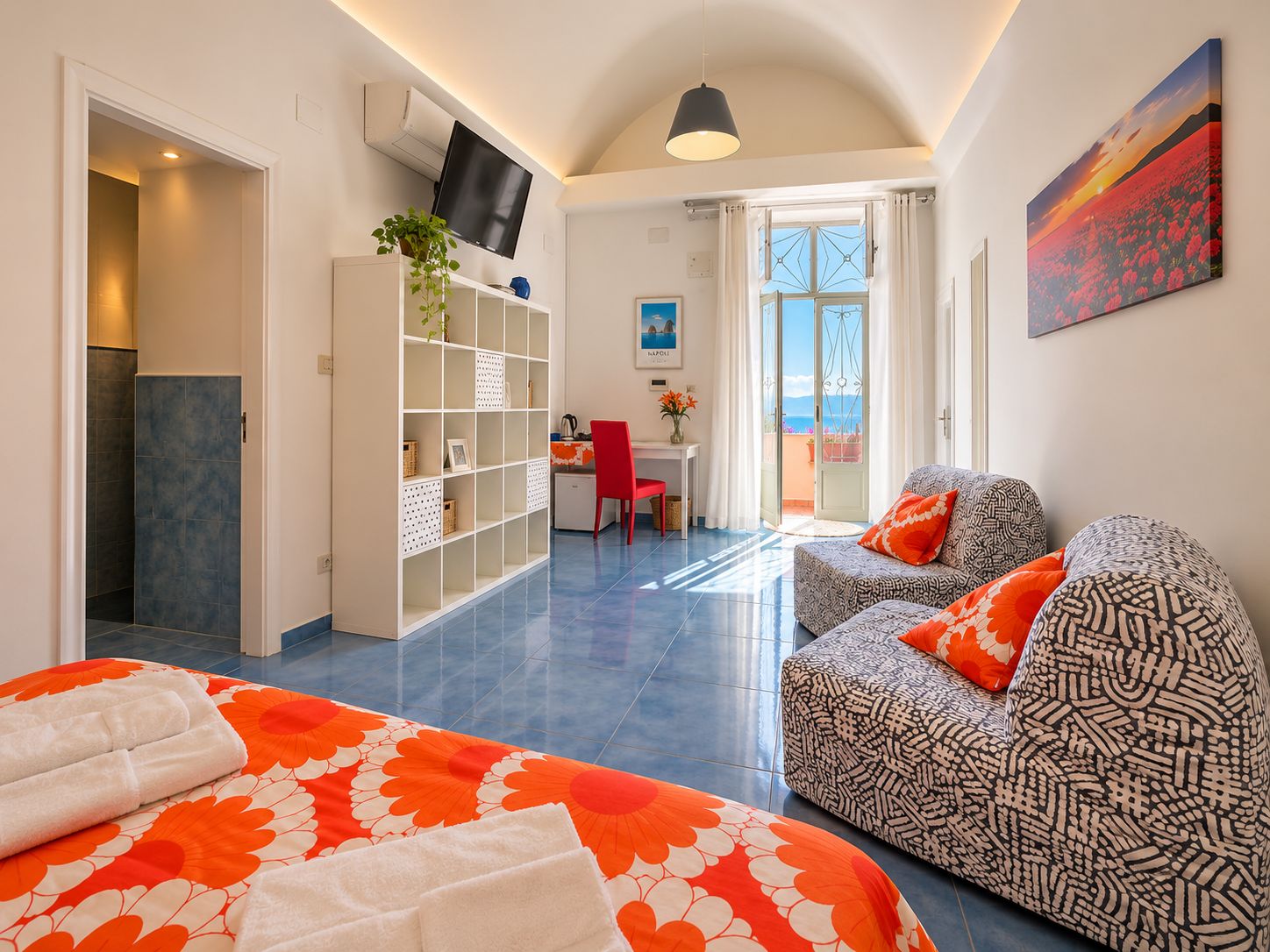 Una camera d'albergo con un letto, un divano, una scrivania e una televisione.