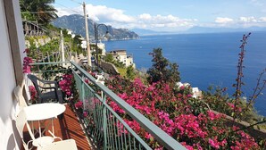 Un balcon avec vue sur la mer, des fleurs roses et une table blanche.