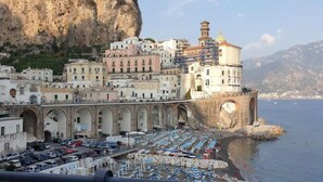 Une ville côtière qui se distingue par un bâtiment historique remarquable, un port de plaisance avec des bateaux et une falaise rocheuse en arrière-plan.