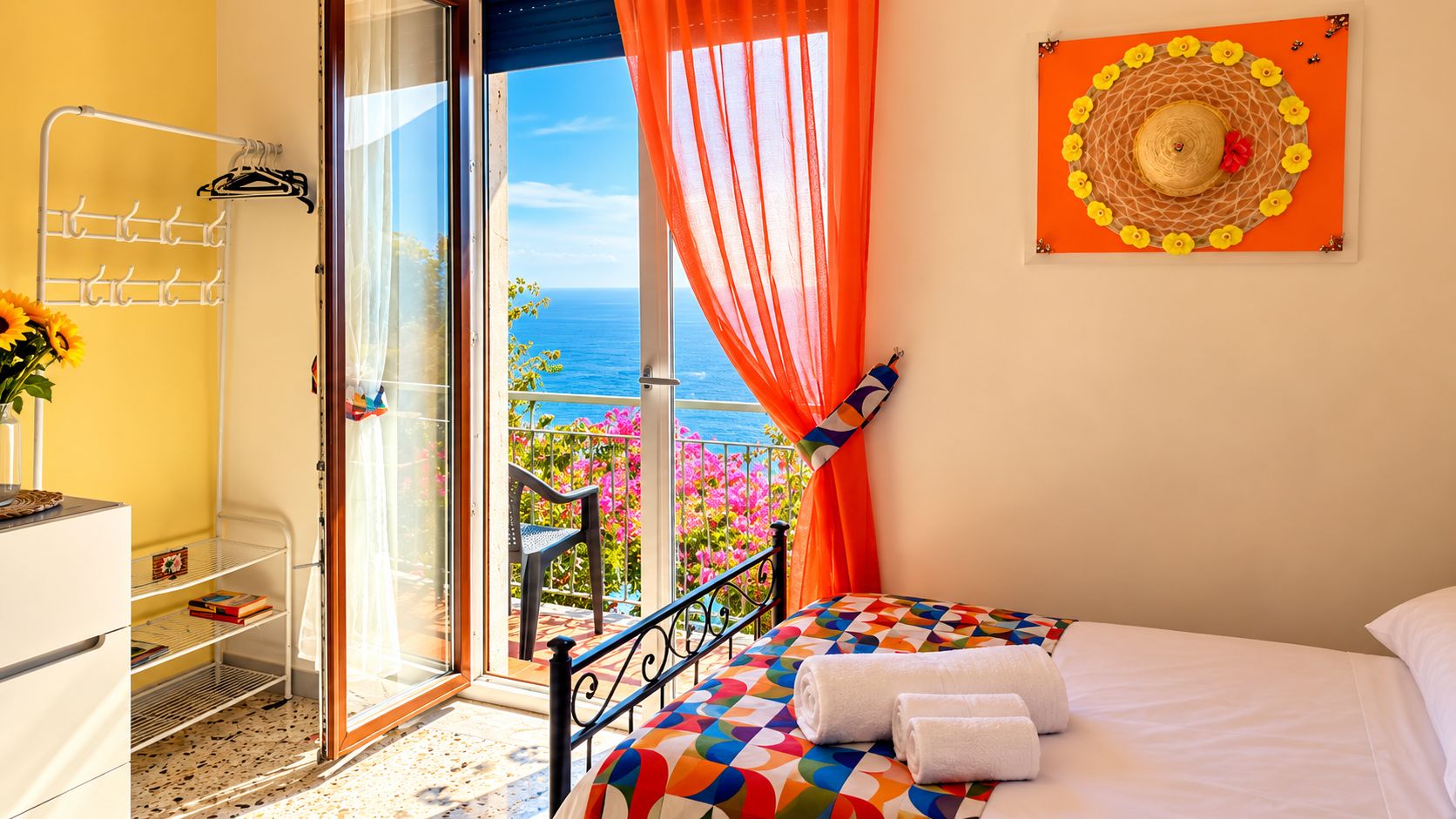 Een slaapkamer met een bed, een raam met uitzicht op zee, een balkon met een stoel en een decoratie aan de muur.