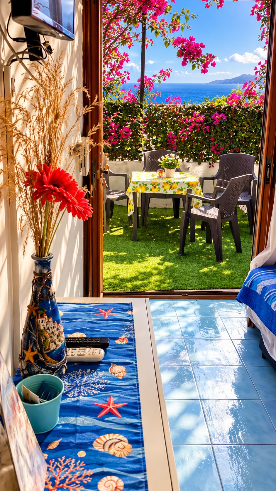Una habitación con vistas al mar, una mesa con sillas, un florero con flores y un suelo de baldosas.