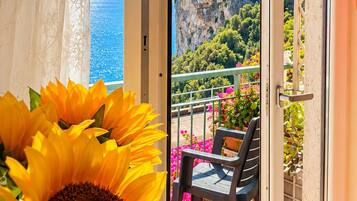Un balcone con vista su una scogliera e il mare, un girasole e una sedia.