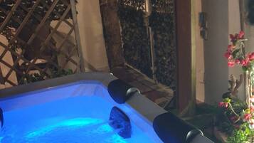 Un jacuzzi con luz azul, rodeado de un jardín con plantas y una cerca metálica.